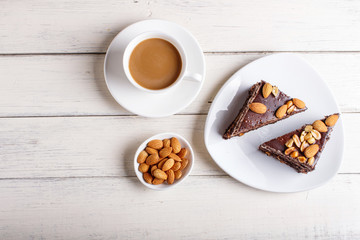 Chocolate cake with caramel, peanuts and almonds on a white wooden background.