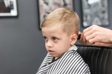 Barber trimming a little boy with blue eyes in a barbershop close-up
