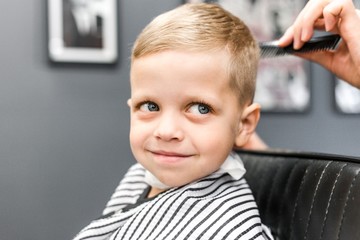 Barber trimming a little boy with blue eyes close-up