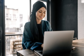 Young Muslim woman working remotely on a laptop sitting in the office
