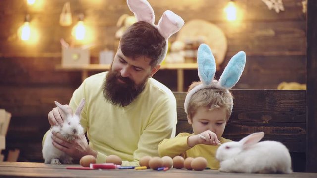 Happy family are preparing for Easter. Cute little child boy wearing bunny ears. Beautiful child boy painting Easter eggs. Father and son paint Easter eggs. Easter hare on a wooden table.