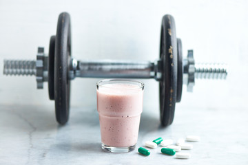 Glass of Protein Shake with milk and raspberries. BCAA amino acids, L - Carnitine capsules and a dumbbell in background. Sport nutrition. Stone / Wooden background. Copy space. 