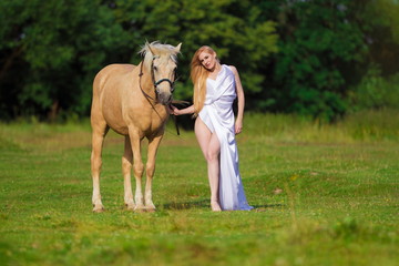 Young rider woman blonde with long hair in a white dress with a train posing and jumping on a...