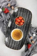 Creme brulee with strawberries on a black plate. Restaurant serving