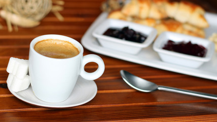 Croissant, cherry marmalade and orange and a cup of coffee on a plate on wooden table