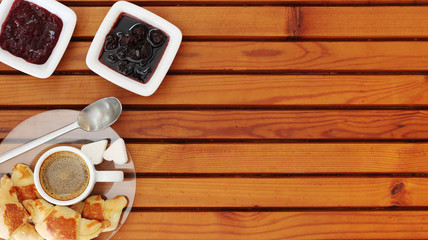 Croissant, cherry marmalade and orange and a cup of coffee on a plate on wooden table