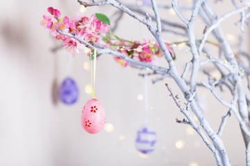 Decorated colorful Easter egg hanging on tree branch indoor with warm bokeh on white background.
