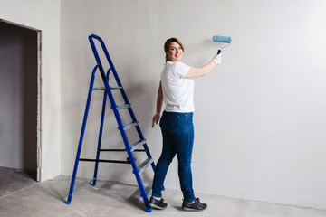 Happy smiling woman with roller in her hand painting interior wall of new house. New flat renovation concept. White background copyspace