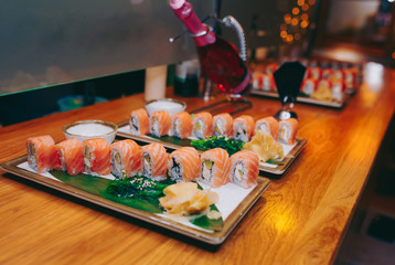 Close-up Sushi plateau Philly buffet in night dining restaurant with bottle of champagne. Delicious Philadelphia fresh seaweed and ginger. Rolls served on plate in a bar. Norwegian salmon and Fish.