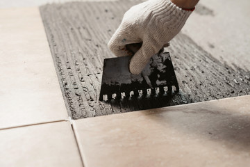 The hands of the tiler are laying the ceramic tile on the floor. Close up macro shot. Home...