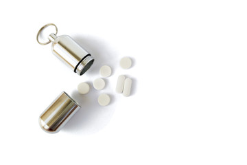 Silver medicine bottle with white pills next to it, isolated on white background. Portable key chain container for pills and small items, useful for hiking, camping, and expeditions.