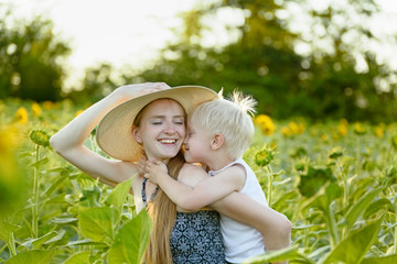 Happy laughing mother giving toddler son piggyback ride on background of green blooming sunflowers...