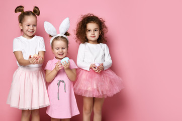 Three smiling dressed up for the holiday kid girls hold painted eggs on Easter day
