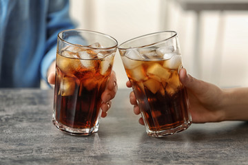 Women holding glasses of cola with ice at table, closeup