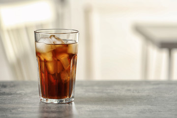 Glass of cola with ice on table against blurred background, space for text