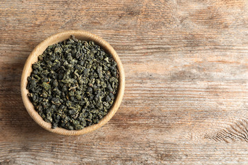 Bowl of Tie Guan Yin oolong tea leaves on wooden background, top view with space for text