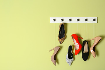 Different lady's shoes hanging on rack against color background, space for text