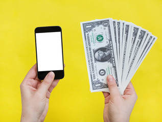 Woman hand holding mobile phone and dollars on yellow background