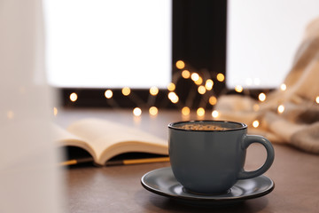 Cup of hot winter drink near window, space for text. Cozy season