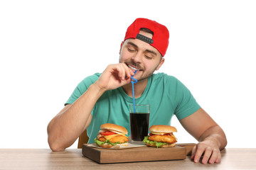 Handsome man having lunch with burgers at table on white background