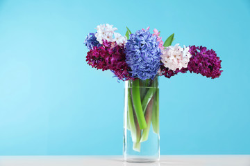 Beautiful hyacinths in glass vase on table against color background, space for text. Spring flowers