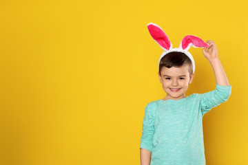 Portrait of little boy in Easter bunny ears headband on color background, space for text