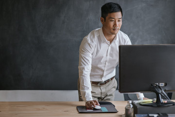 Asian businessman standing at his desk working on a computer