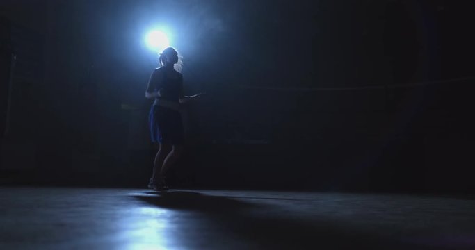 Training girl fighter jumping rope in a dark room