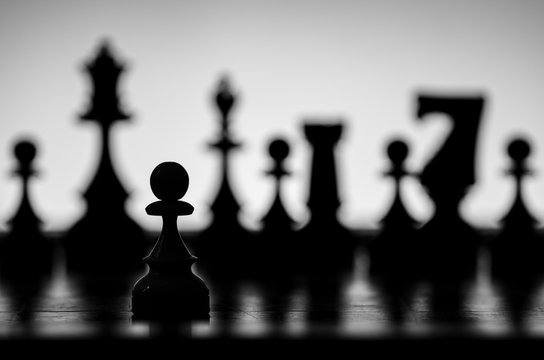 Black and White  Pawn Chess Piece with Oponnent Pieces out of Focus in Silhouette