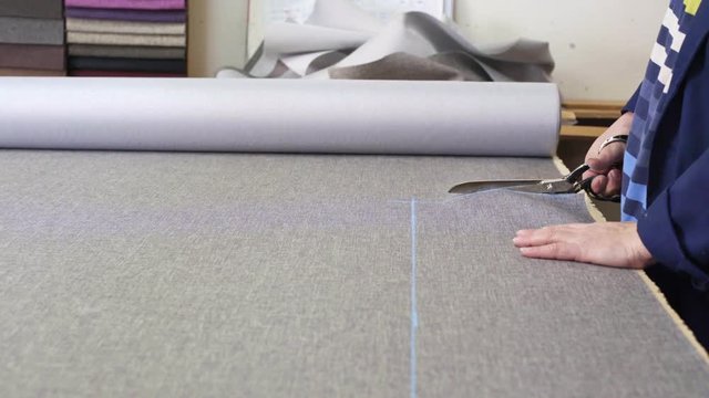 Closeup of an older woman in a furniture factory who is cutting a grey material for the sofa