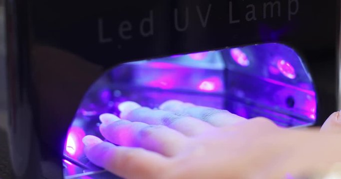 Close-up of beautiful female hand with white nails under the lamp for polymerization and extension.