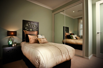 Modern bedroom with green paint and wooden backboard with a beige quilt
