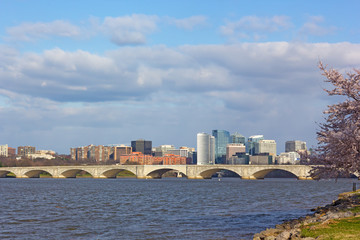 Fototapeta premium Arlington Memorial Bridge across Potomac River during cherry blossom season. Urban landscape of Arlington neighborhood skyscrapers, Virginia, USA.