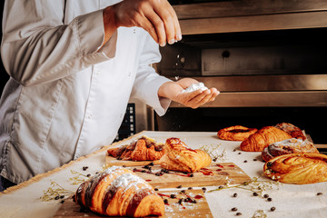 Baker topping croissants and puffs with sugar powder