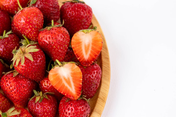Strawberrys many with both ripe fruit and  not fruit ripe, have half strawberry place above in wooden tray, strawberrys and wooden tray all laid are on a white background.