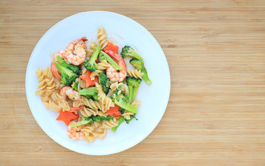 Fried Spiral Macaroni with shrimp and vegetables on white plate against wooden board background.