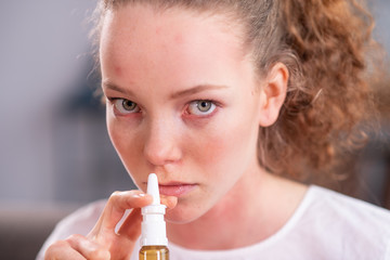 Beautiful young lady with light green eyes spraying medicine