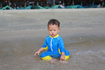 Portrait of Asian baby boy in swimming suit sitting on the sand beach.