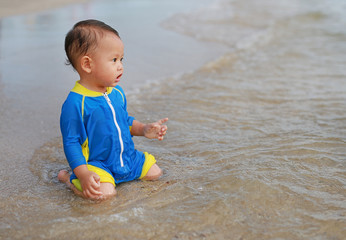 Portrait of Asian baby boy in swimming suit sitting on the sand beach.