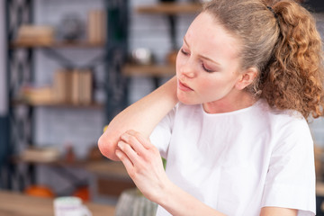 Distressed unhappy young lady rubbing her spotted elbow
