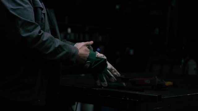Man putting on working gloves in industrial, dark workshop.