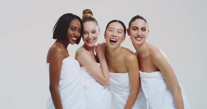 Slow motion of beautiful young women of different ethnicities with perfect firm and slim body in white bathing towels having fun and laughing in camera isolated on white background. 