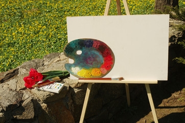 A frame, blank canvas and palette against the background of green grass and flowers. Sketch on...