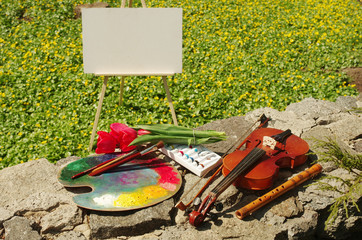 Violin, stretcher, empty canvas and palette against the background of green grass and flowers. Art in nature