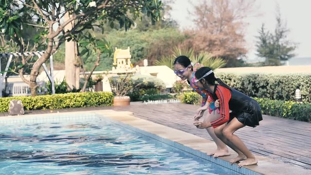 Asian girls wearing goggles and jumping in pool in sunny day together, slow motion.