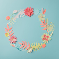 Colourful handmade tropical paper flowers and leaves on blue pastel background with copyspace, seasonal easter wreath, summer spring flower, papercraft origami idea