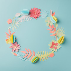 Colourful handmade tropical paper flowers and leggs on blue pastel background with copyspace, seasonal easter wreath, summer spring flower, papercraft origami idea