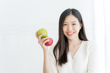 Fototapeta na wymiar Young Asian woman showing green apple and red apple, indoors portrait