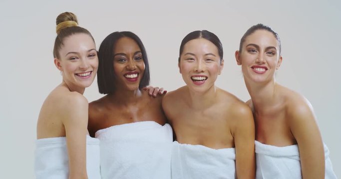 Slow motion of beautiful young smiling women of different ethnicities with perfect firm and slim body in white bathing towels dancing and having fun isolated on white background. 