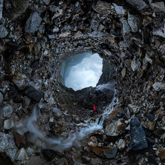 man in red stands under a waterfall on a black rock in the mountains on a cloudy rainy day. Tiny...